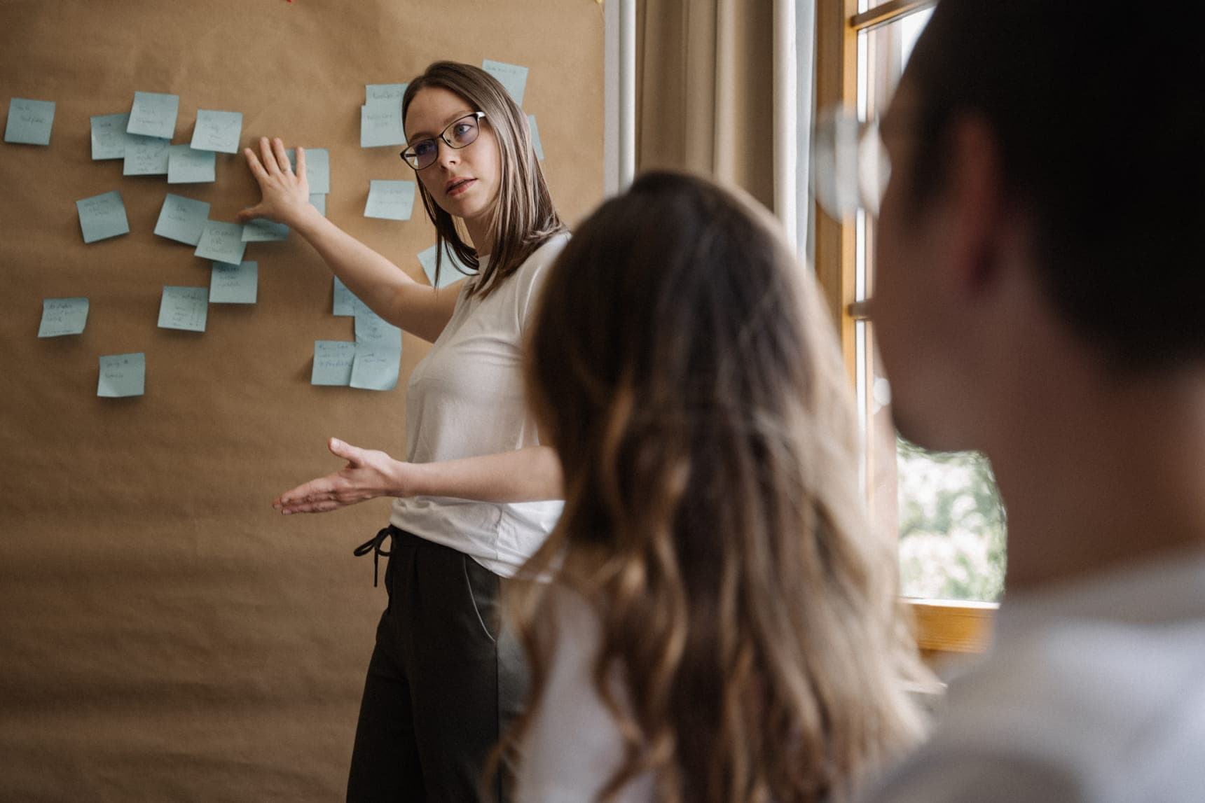 A woman presents ideas in front of a wall covered with sticky notes while seated colleagues listen nearby.