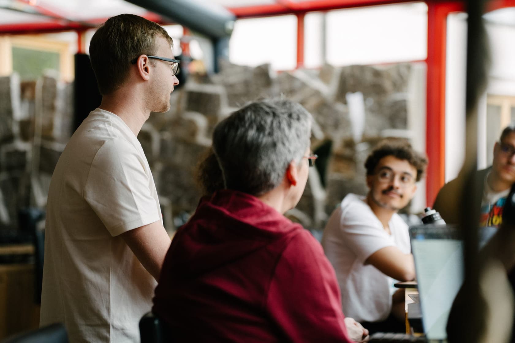 A group of colleagues engaged in a discussion in a room with rough stone walls and red structural beams.