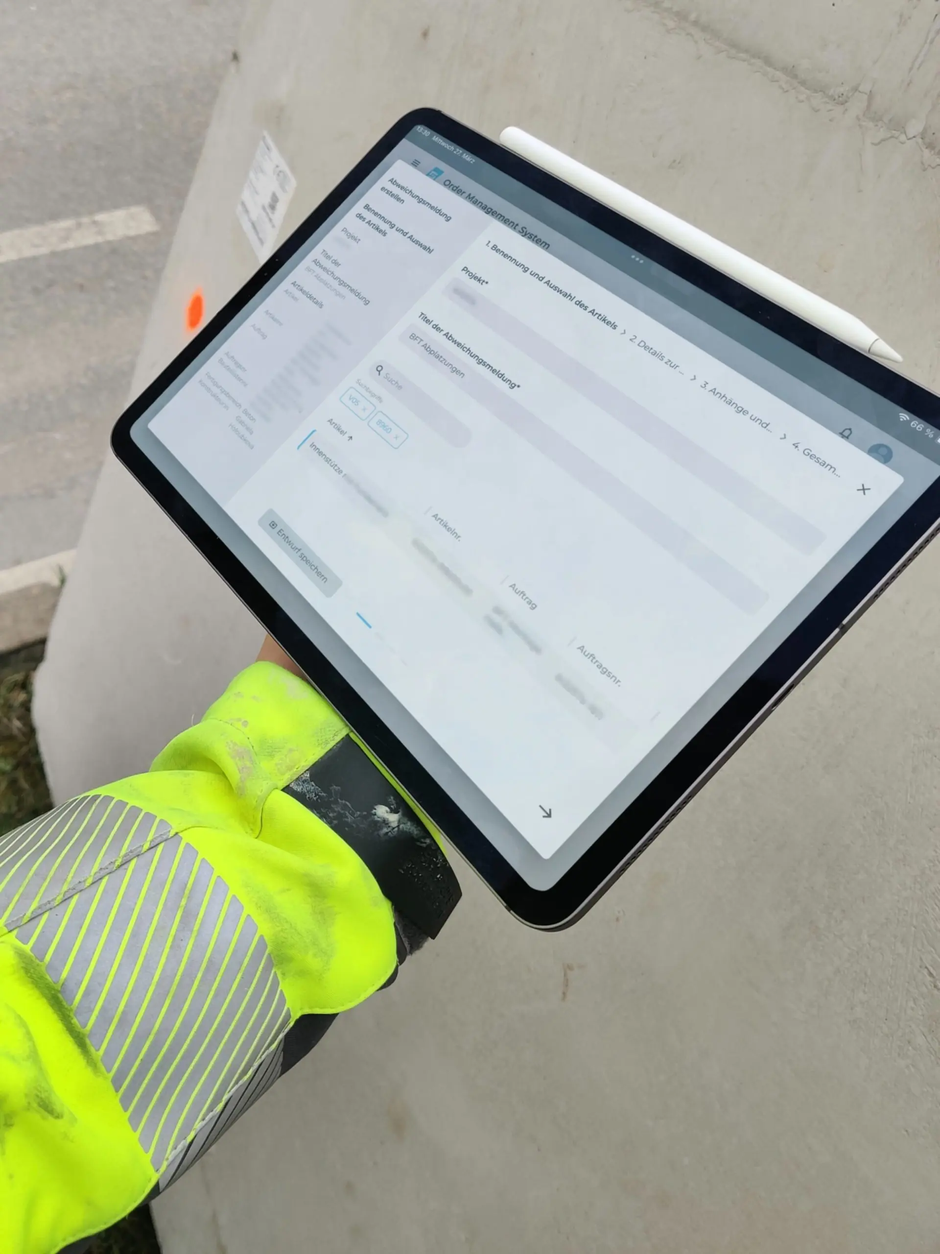 A person wearing a high-visibility jacket holds a tablet displaying an "Order Management System" form with fields including "Projekt," "Titel der Abweichungsmeldung," and a multi-step workflow, outdoors on a construction site.