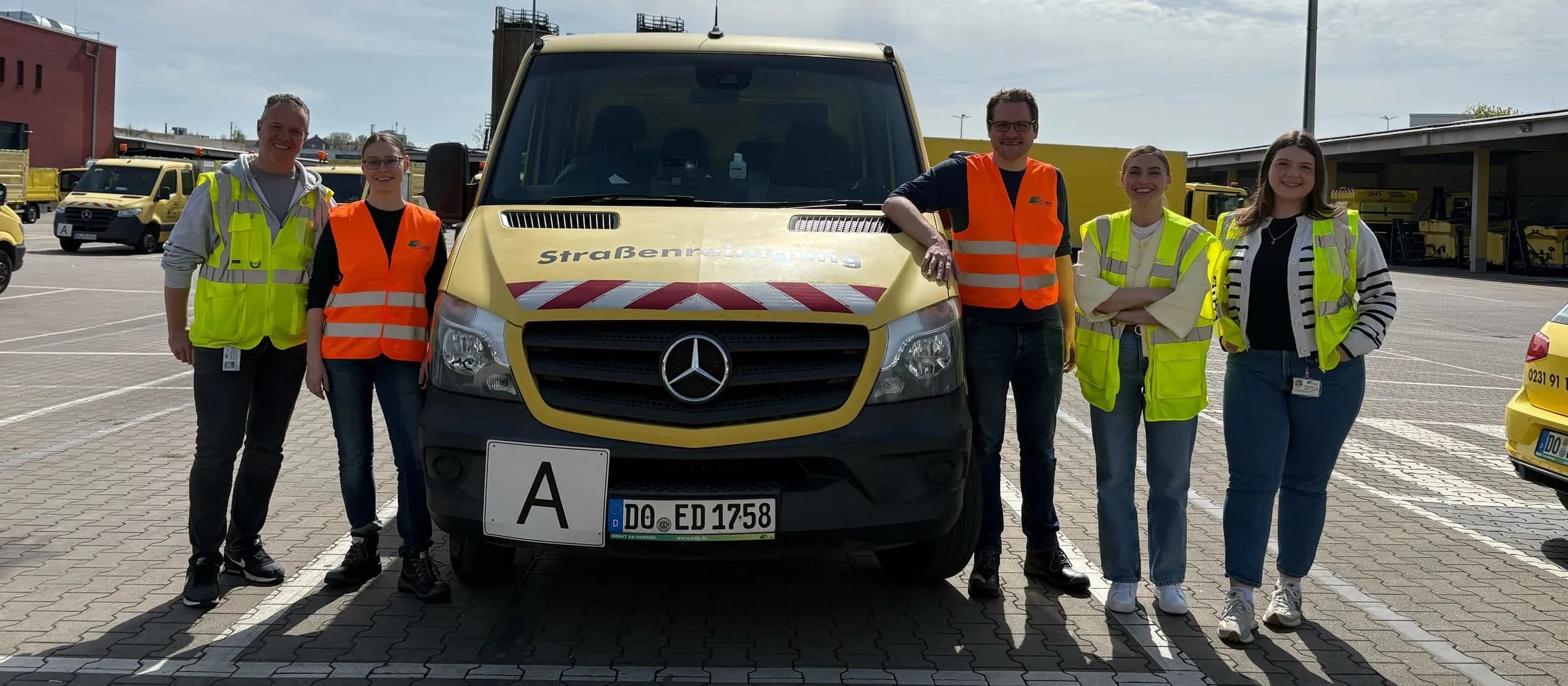 Five people in high-visibility vests standing at the EDG depot in front of a yellow van labelled Straßenreinigung (street cleaning)