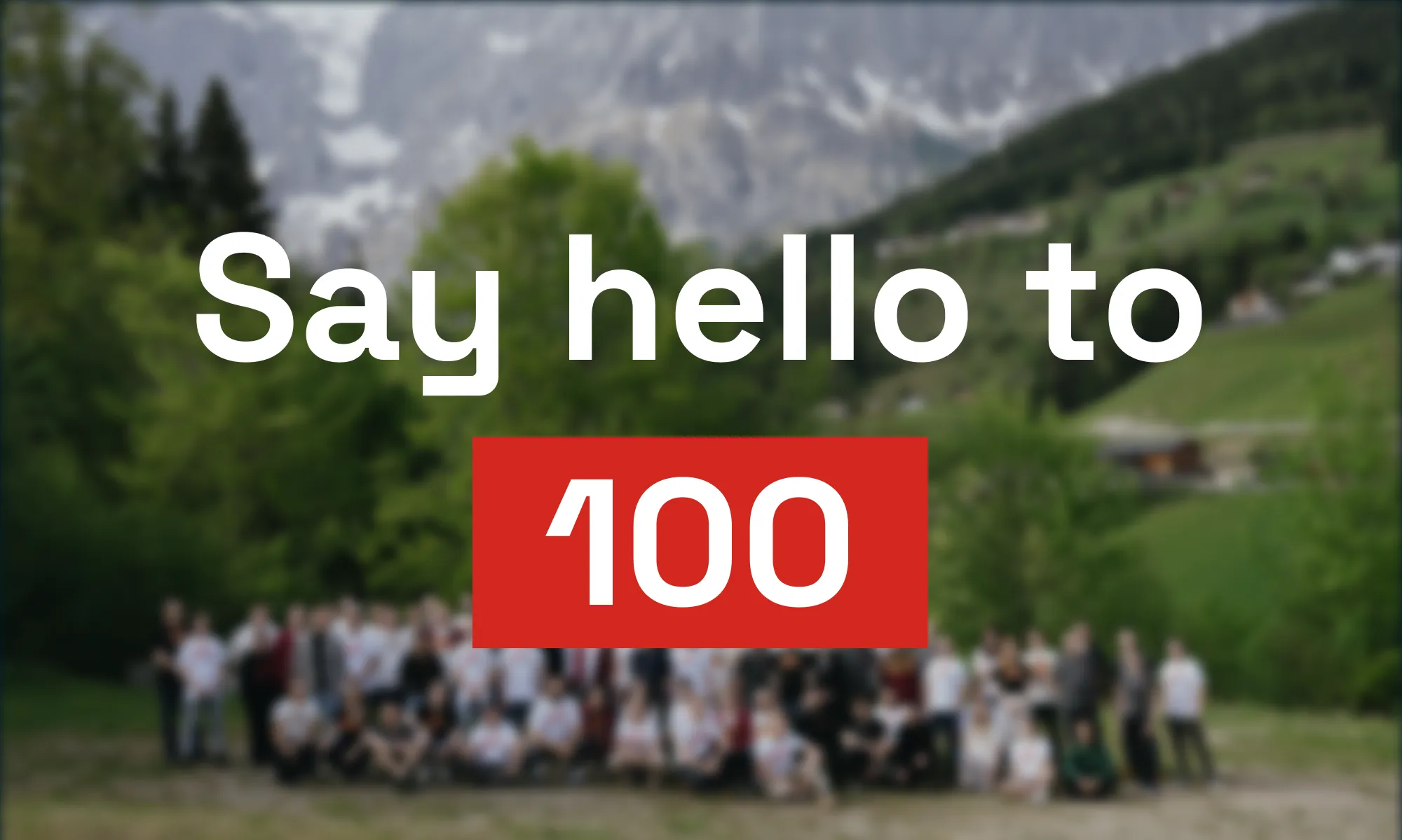 Text reading "Say hello to 100" over a blurred group photo of many people posed outdoors in an alpine landscape with mountains and green trees.