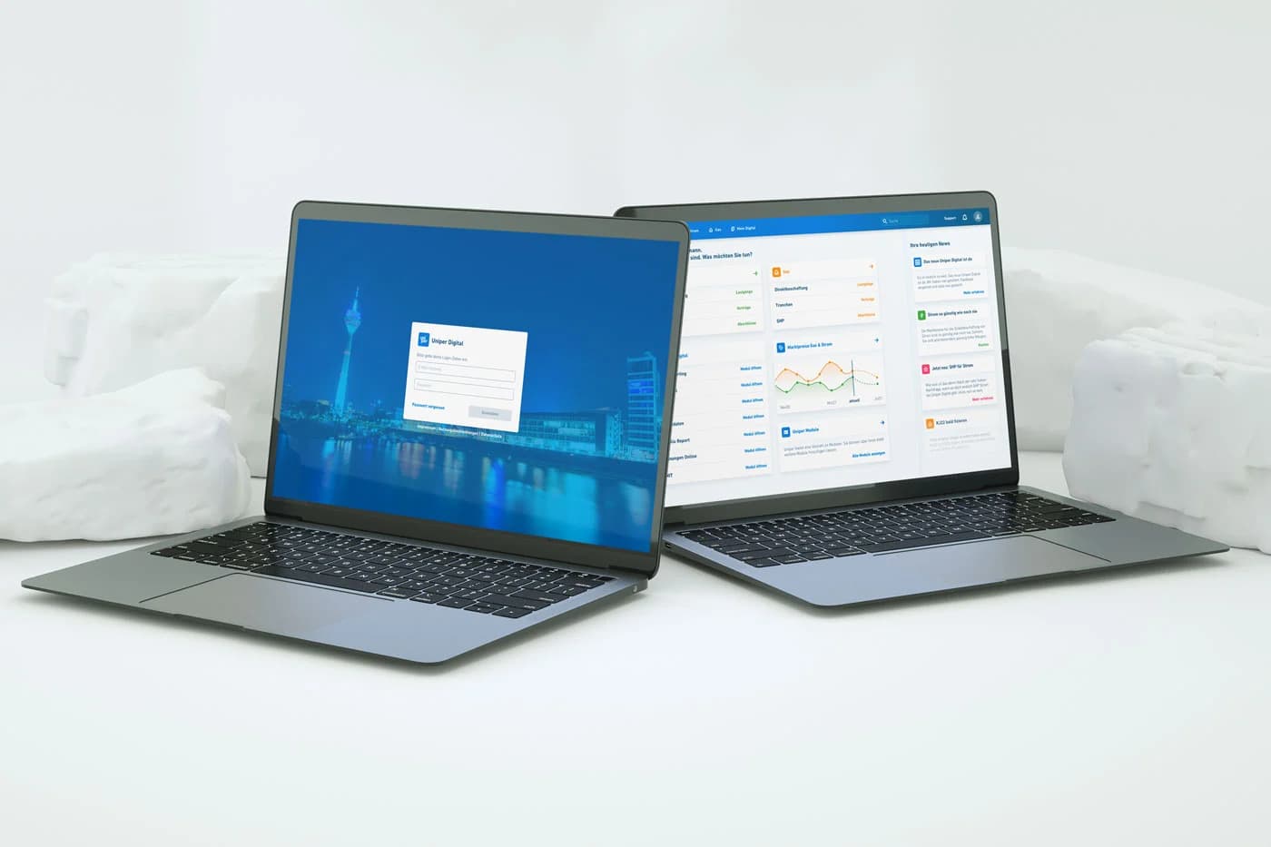 Two grey laptops on a white surface with abstract white blocks, showing the Uniper Digital web platform — one screen displays a login form with a Düsseldorf skyline background, the other shows a dashboard with energy market data, charts, and a news feed.