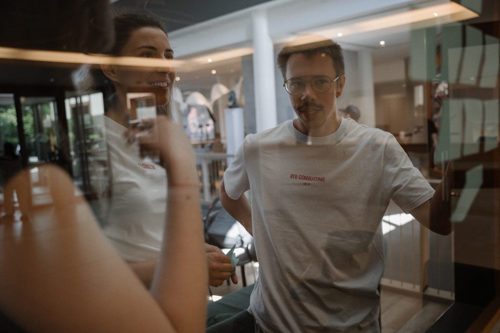 A colleague in an iits consulting t-shirt holding a door handle, with another team member holding a green origami crane in the background.