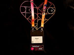 KotlinConf 2025 t-shirt with neon heart logo and the badge of Robert Wloch with collected pins on the band while diving into the Kotlin ecosystem