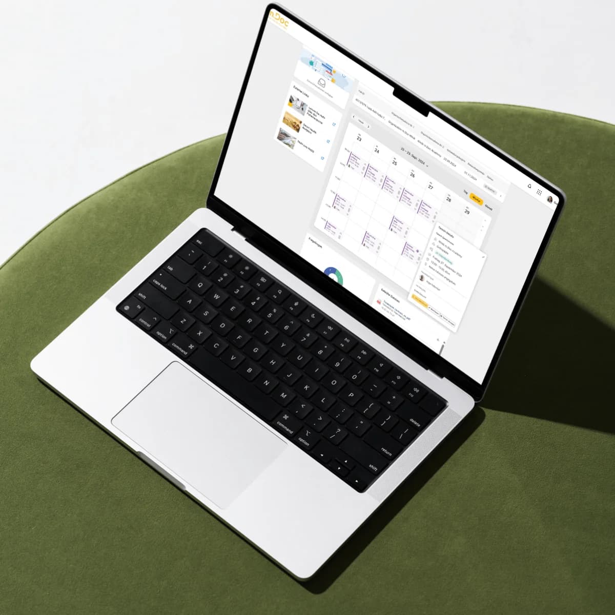 Laptop resting on a green upholstered surface displaying the M.Doc application interface, showing a weekly calendar view with dates 23–29 and overlapping dashboard panels.