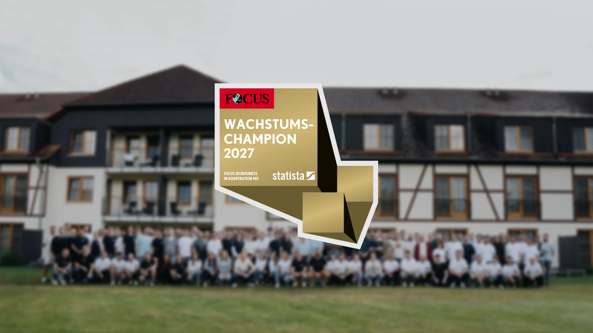 FOCUS Wachstums-Champion 2027 award badge, issued by focus.de/business in Kooperation mit Statista, overlaid on a blurred group photo of many people standing in front of a large building.