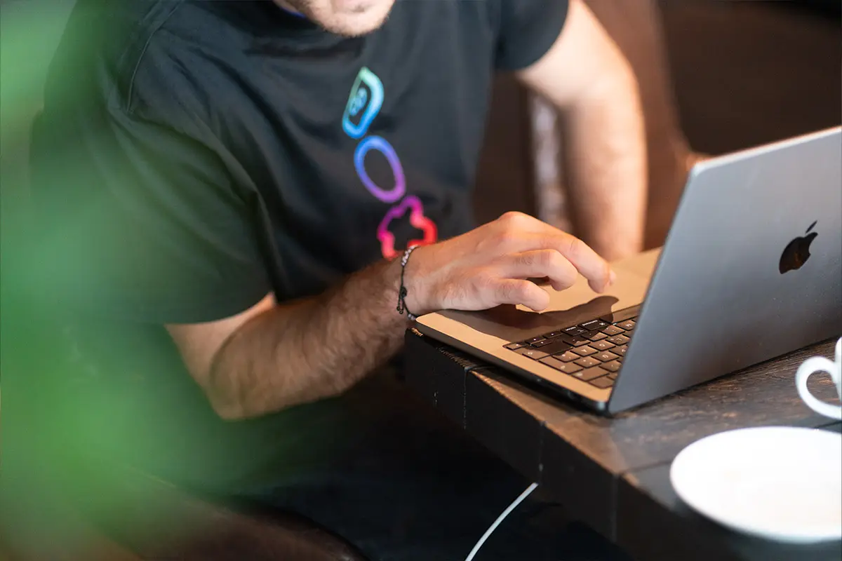 Close-up of a man's hands typing on a laptop keyboard, wearing a t-shirt with a colorful geometric logo.