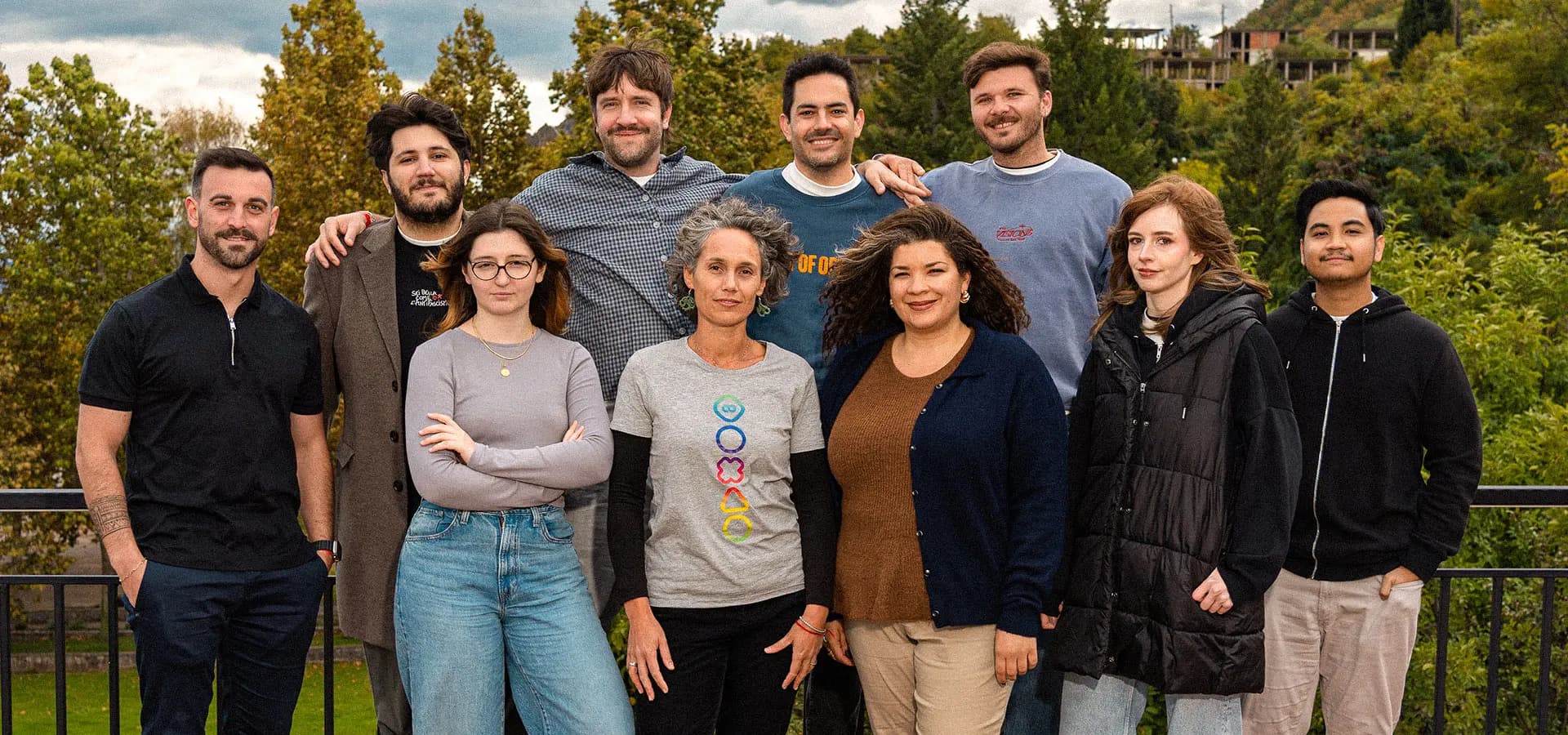 A group photo of the 8reasons digital team, consisting of ten people standing on an outdoor terrace with a railing. The team members are arranged in two rows, smiling at the camera, with a background of lush green trees and a hillside under a cloudy sky.